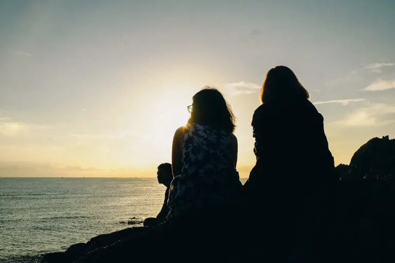 Två kvinnor som är bästa vänner och sitter på en strand tillsammans i solnedgången