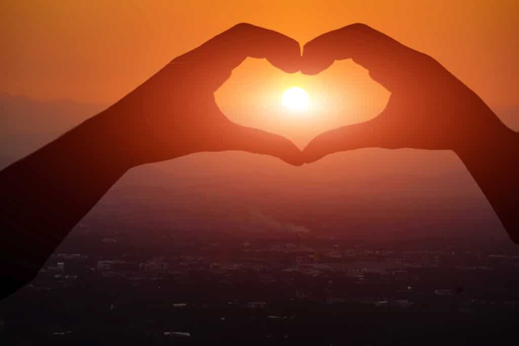 Person som utövar tacksamhet genom att hålla upp ett handhjärta mot solen