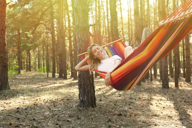 En glad kvinna som ligger i en hängmatta skogen och ler
