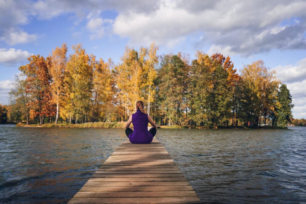 Kvinna som ägnar sig åt meditation på en brygga vid en sjö