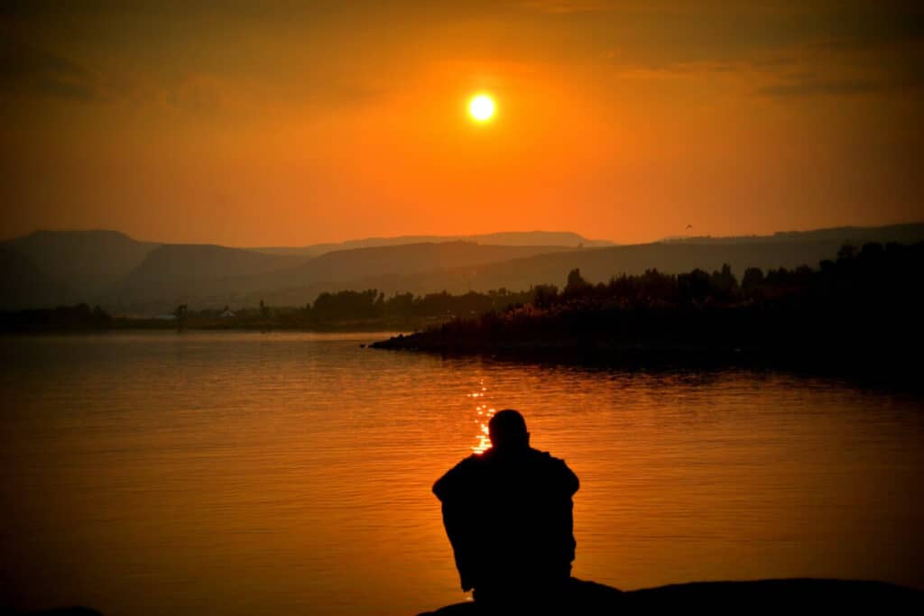 Introvert person som sitter och blickar ut över en sjö i solnedgången
