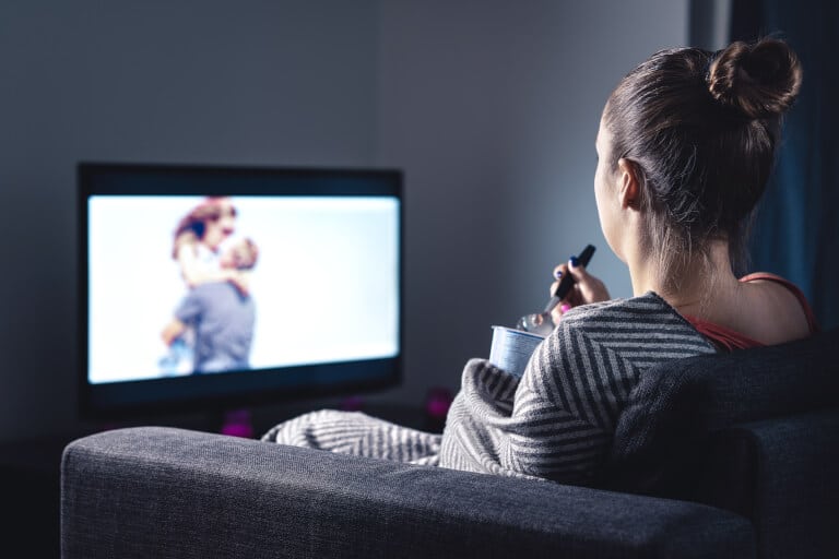 Kvinna som sitter i soffan och äter glass medan hon tittar på en romantisk film på tv:n