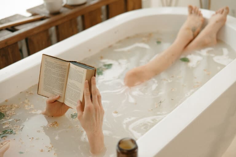 Kvinna som badar i badkaret och samtidigt läser en bok